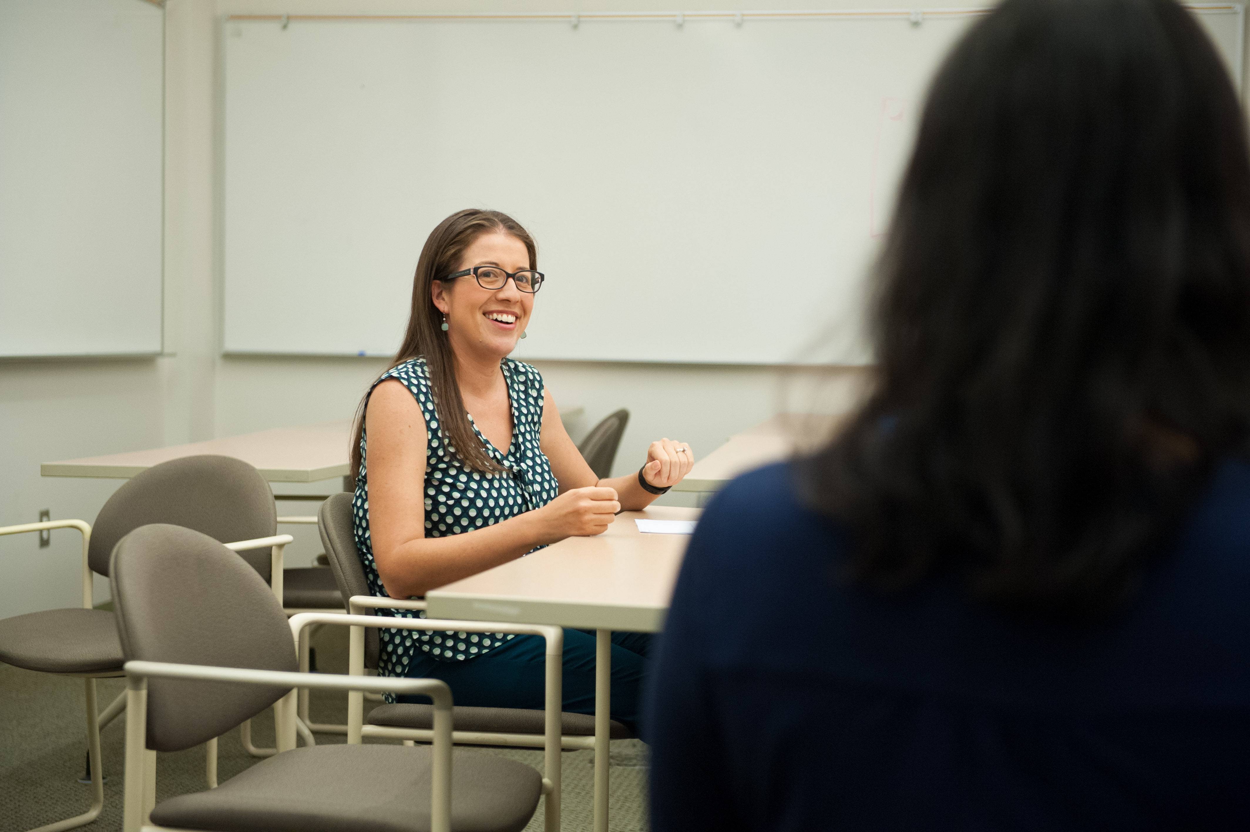a person sitting at a table with a whiteboard in the background